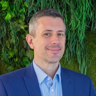 Photograph of a smiling man in blue suit before a green plant wall