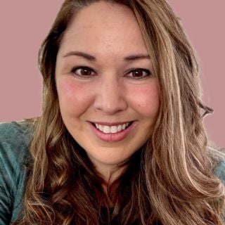 Photograph of smiling woman with long wavy brown hair, green top, pink background