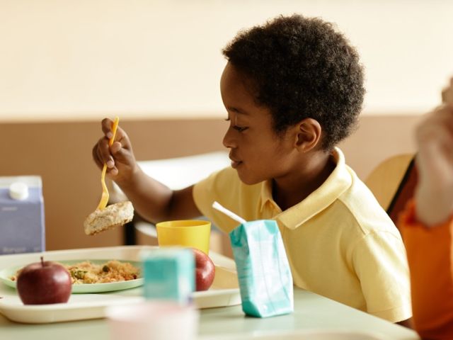 Photo: young boy in yellow shirt eating from a tray with apple and juice carton