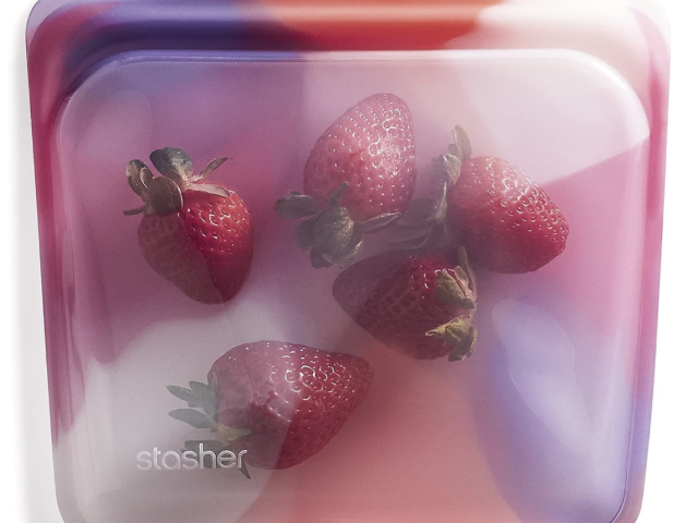 Photograph: translucent Stasher silicone bag holding five strawberries, pink-purple gradient