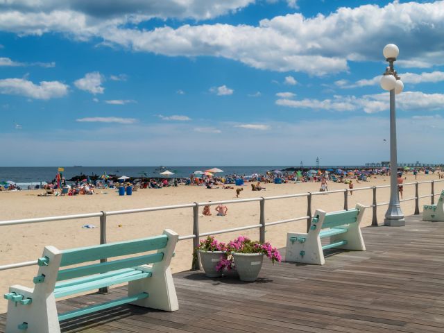 Sunny boardwalk with mint-green benches, lampposts and crowded sandy beach