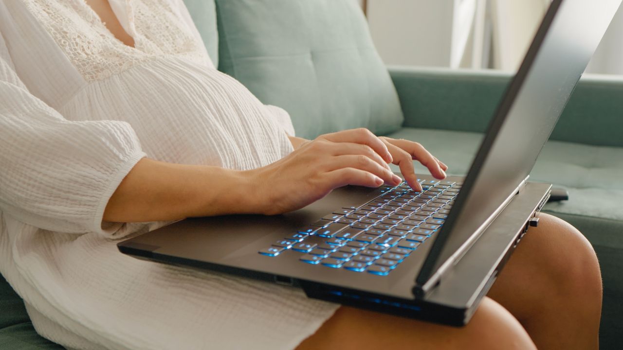 Pregnant woman in white dress typing on a laptop
