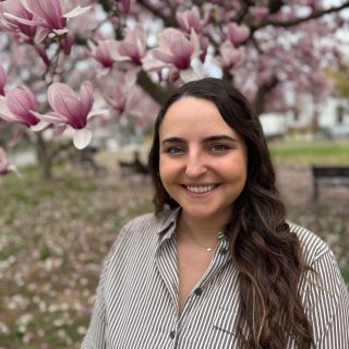 Young woman with long hair smiles amid blooming magnolia trees in a park.