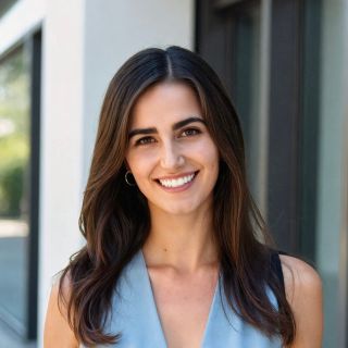 Smiling woman with long brown hair, wearing a light blue top, standing outdoors.