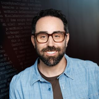 Photograph: smiling bearded man with glasses in blue shirt, dark background with code text
