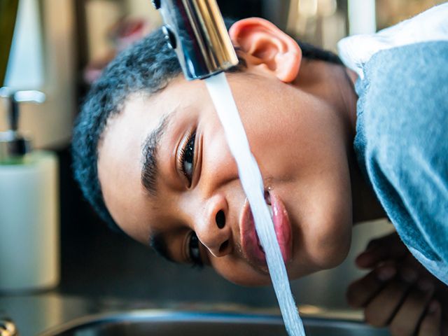 A person drinking from a faucet