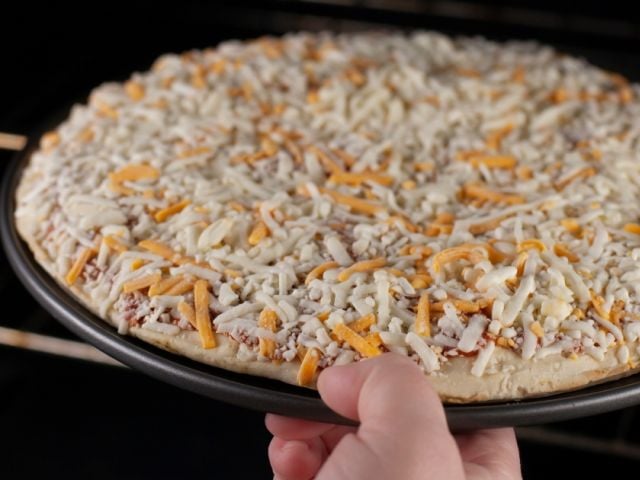Person putting frozen pizza in oven