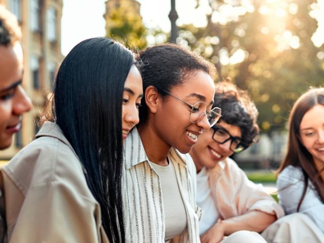 A diverse group of young adults smiling and engaged in conversation outdoors.