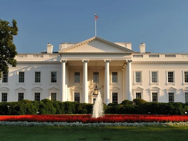 The White House with a manicured lawn and colorful flower beds in front.