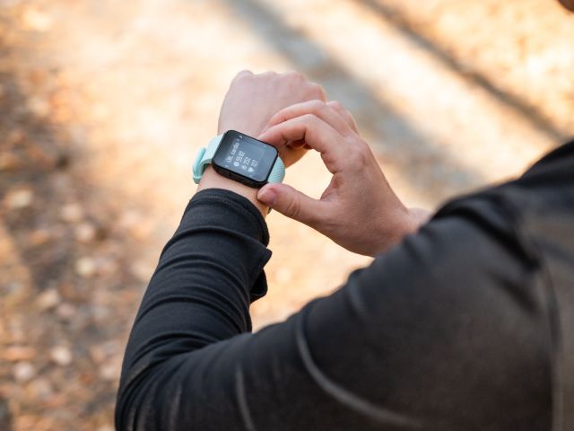 A person adjusting a smartwatch on their wrist, with a forest path in the background.