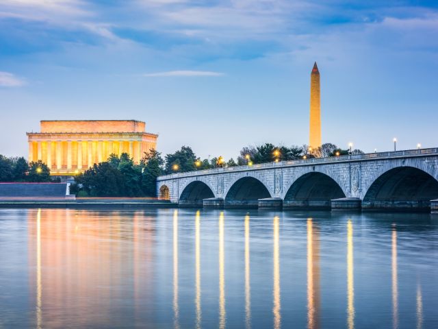 Lincoln Memorial and Washington Monument illuminate at dusk, reflected in calm water.