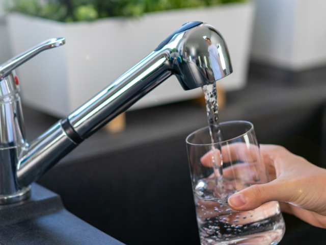 A hand holds a glass under a shiny kitchen faucet as water flows into the glass.
