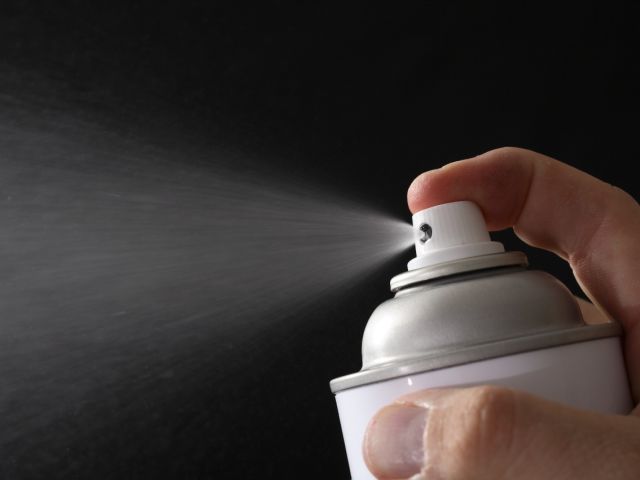 A hand holding a spray can, mist dispersing against a dark background.