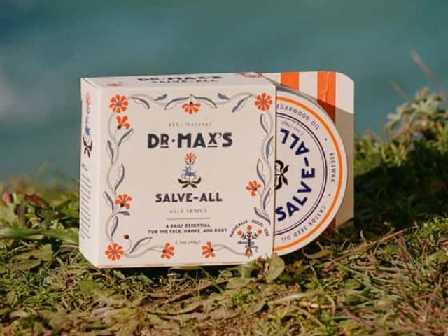 A decorative box of Dr. Max's Salve-All positioned on green grass near a body of water.