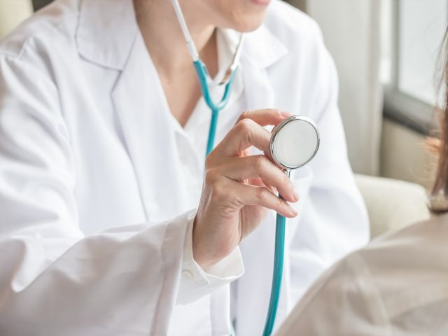 A healthcare professional holds a stethoscope, preparing to examine a patient.