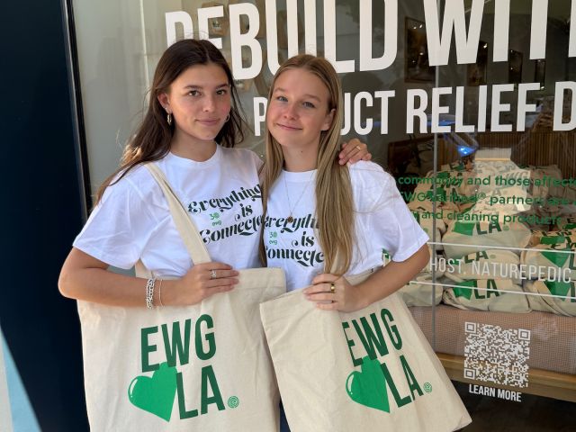 Two young women pose in front of a store, holding tote bags with the text "EWG LA."
