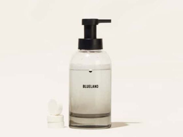 Clear glass bottle with a black pump, labeled "BLUELAND," beside a white tablet.