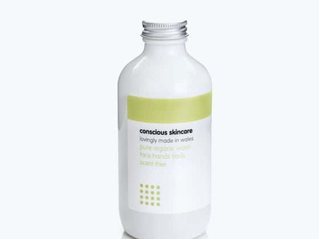 White cosmetic bottle with a green label, labeled "conscious skincare."