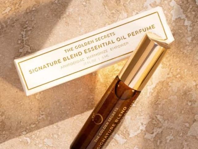 Brown glass bottle of essential oil perfume beside its white box on a textured surface.