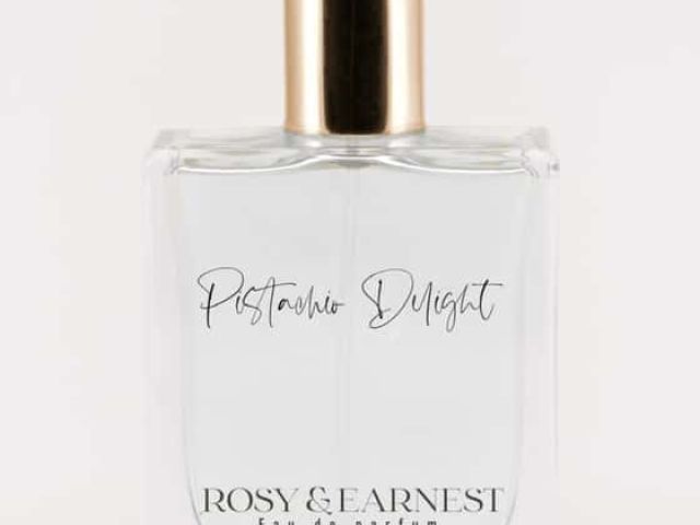 Clear perfume bottle with gold cap, labeled "Postcard Delight" by Rosy & Earnest.