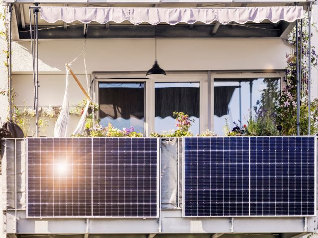 A balcony with solar panels, plants, and a hammock, sun reflecting off the panels.
