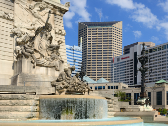 Photograph of a cascading stone fountain and sculptures with downtown skyscrapers