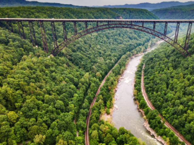 Aerial photograph: steel arch bridge spanning lush green gorge and winding river