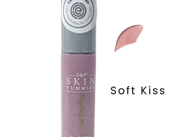 A lavender lip gloss tube with a soft pink swatch beside it, labeled "Soft Kiss."