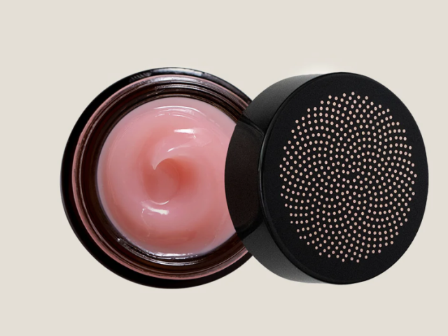 A jar of light pink cream with a dotted black lid, open to reveal a smooth texture.
