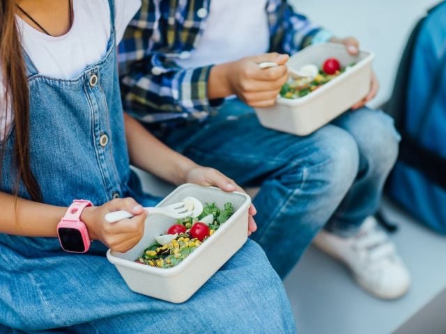 Photo of two children sitting and eating salads from lunchboxes