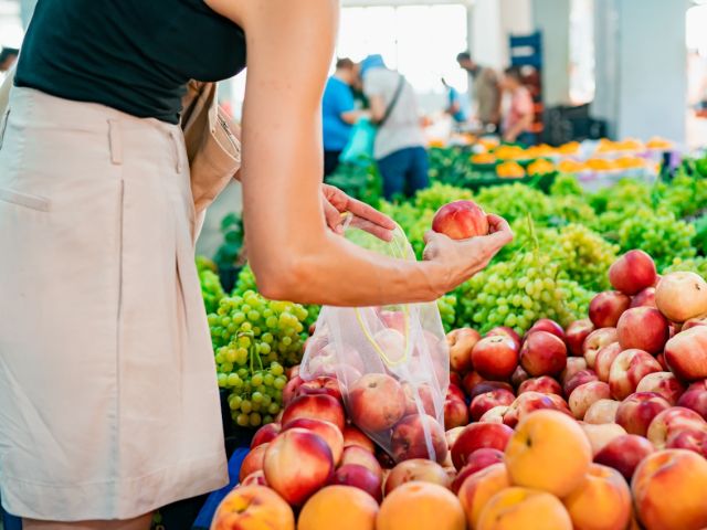 Photograph: person placing nectarines into a bag at a produce stall with grapes