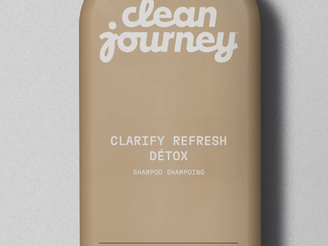 Photograph of beige shampoo bottle with "clean journey" logo and black cap on gray background
