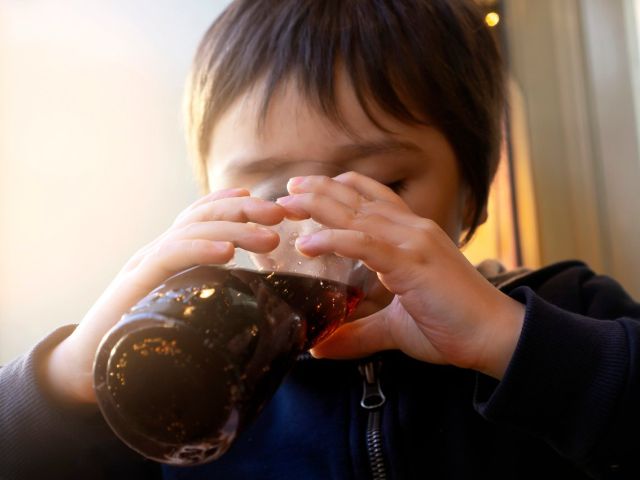 Photo of a child drinking cola from a glass bottle in warm indoor light