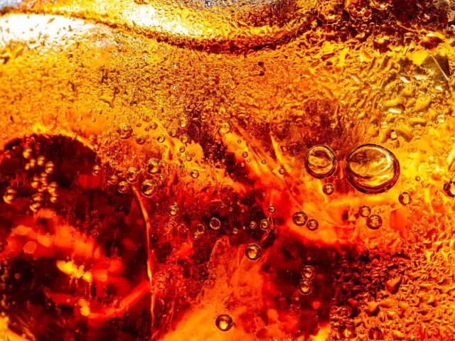 Macro photograph of amber liquid with suspended bubbles and textured surface