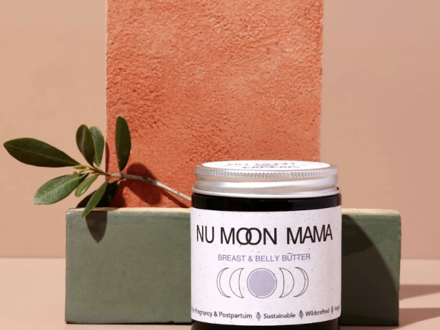 Photograph: jar of Nu Moon Mama breast &amp; belly butter on stacked blocks with green sprig