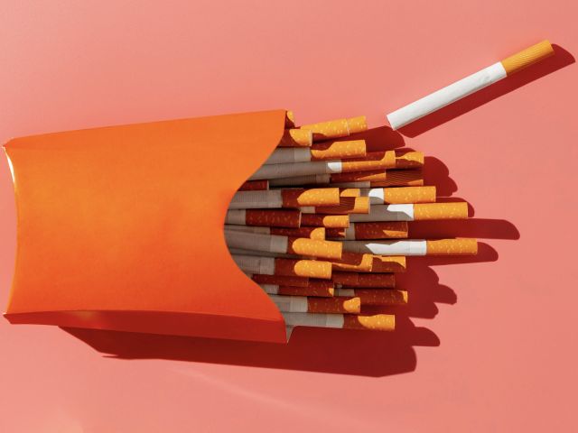 Photograph: orange pack overflowing with cigarettes on coral background, one loose