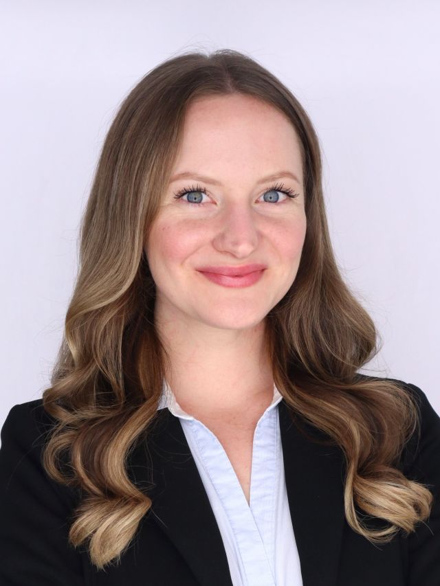 Photograph of smiling professional woman with wavy brown-blonde hair, black blazer