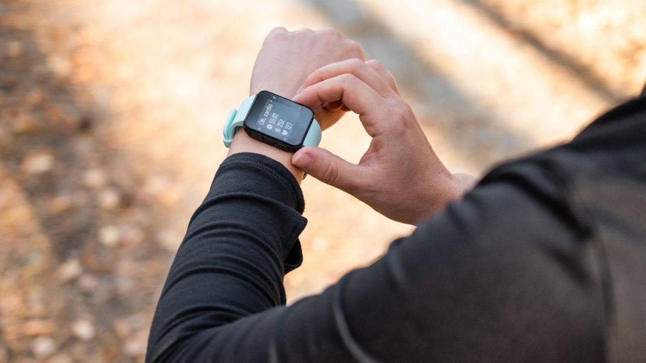 A person adjusting a smartwatch on their wrist, with a forest path in the background.