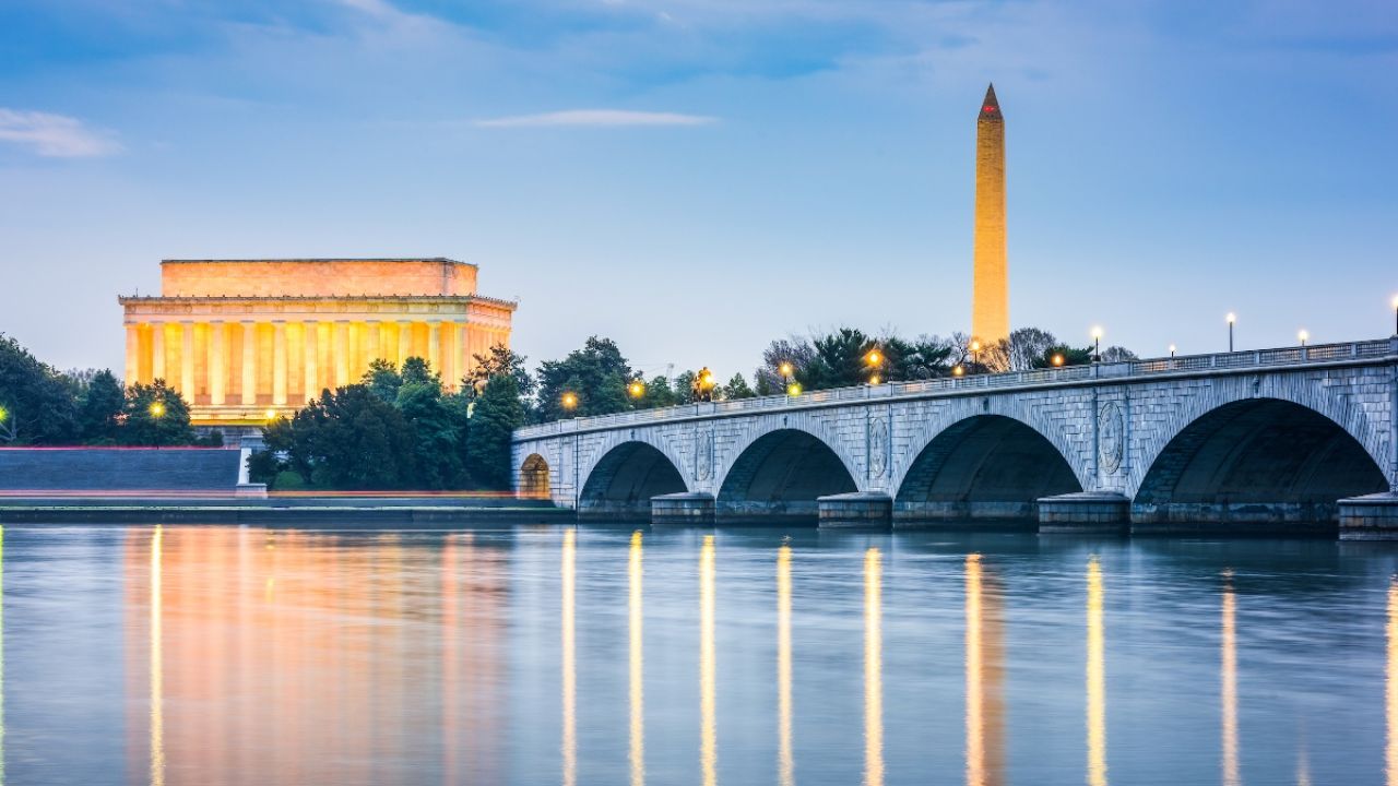 Lincoln Memorial and Washington Monument illuminate at dusk, reflected in calm water.
