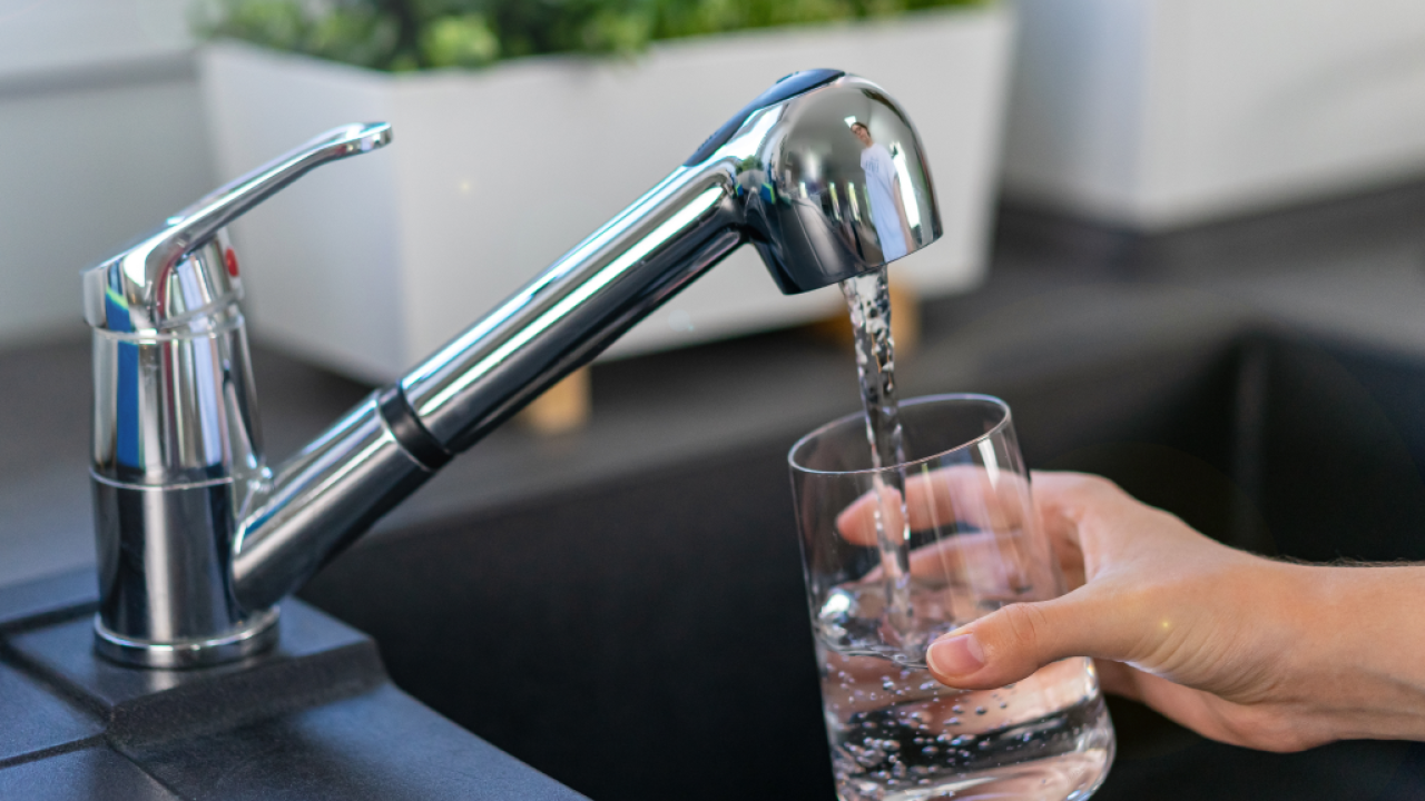 A hand holds a glass under a shiny kitchen faucet as water flows into the glass.