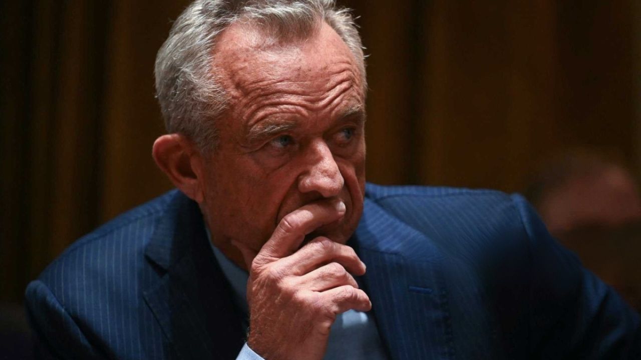 Man in a dark suit with silver hair, deep in thought, seated with hand to chin.
