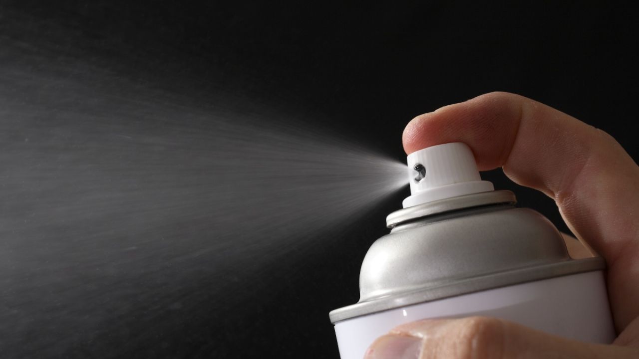 A hand holding a spray can, mist dispersing against a dark background.