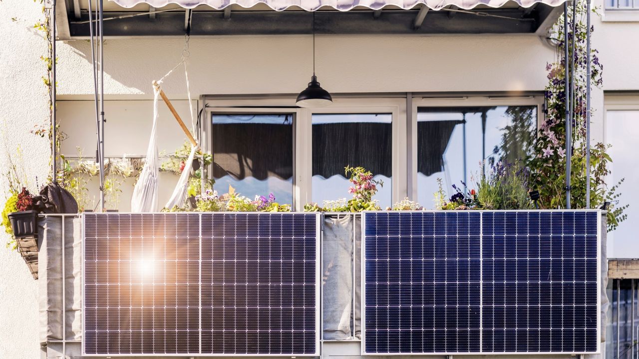 A balcony with solar panels, plants, and a hammock, sun reflecting off the panels.
