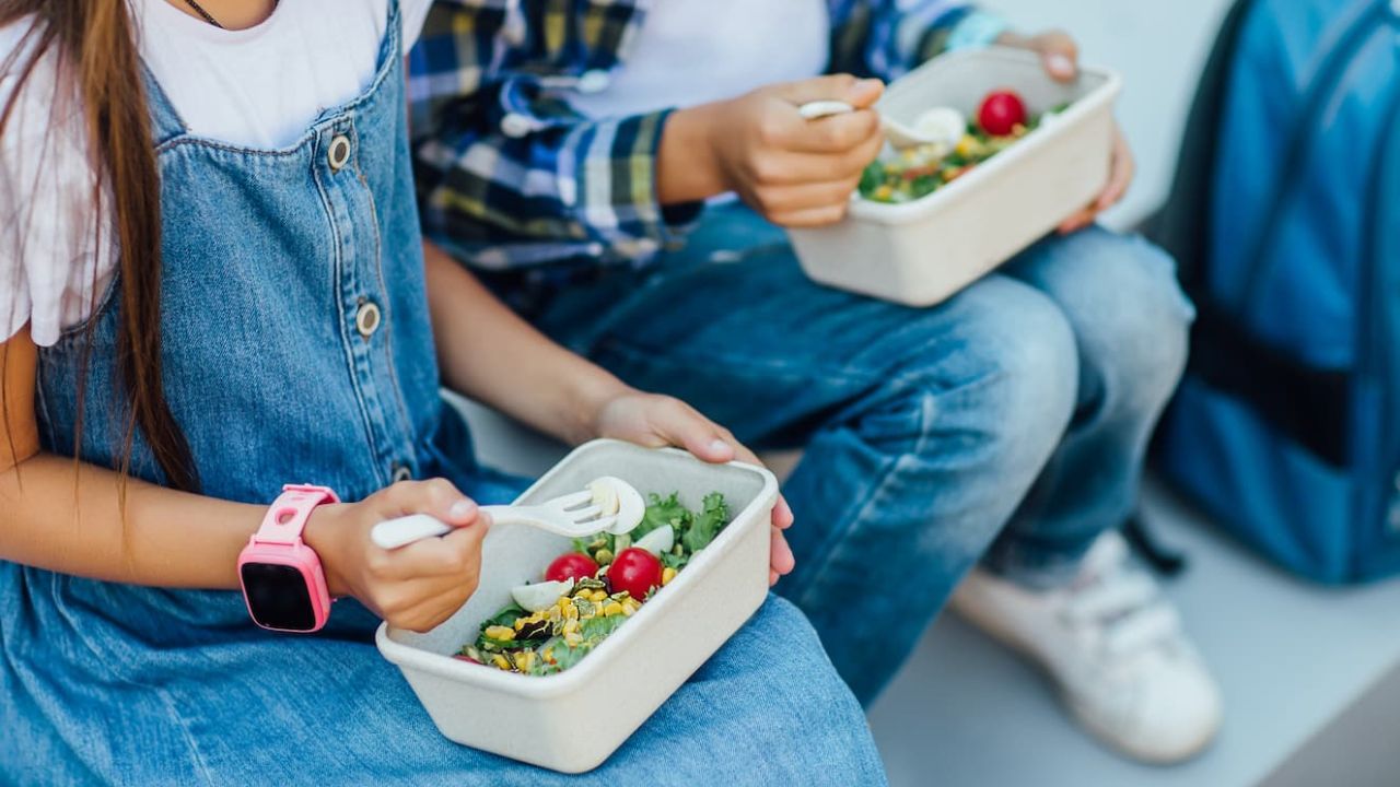 Photo of two children sitting and eating salads from lunchboxes