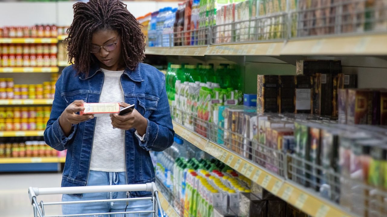 Photograph: woman reading product label in grocery aisle, pushing cart