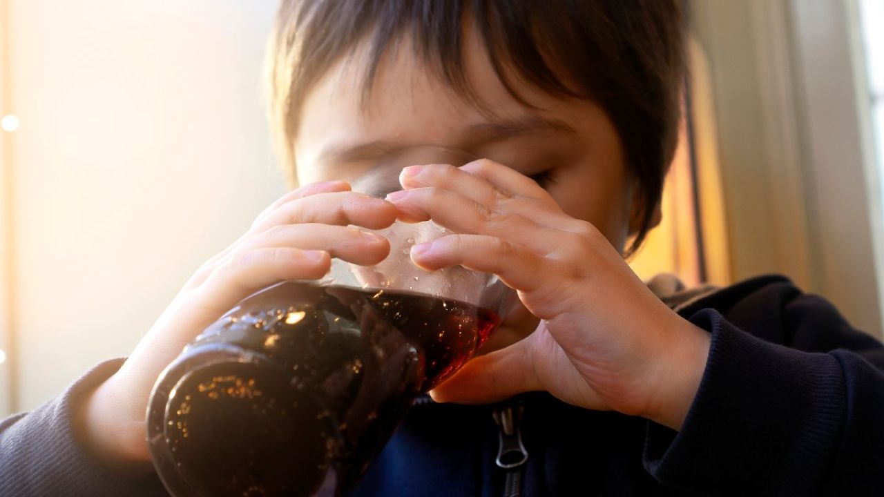 Photo of a child drinking cola from a glass bottle in warm indoor light
