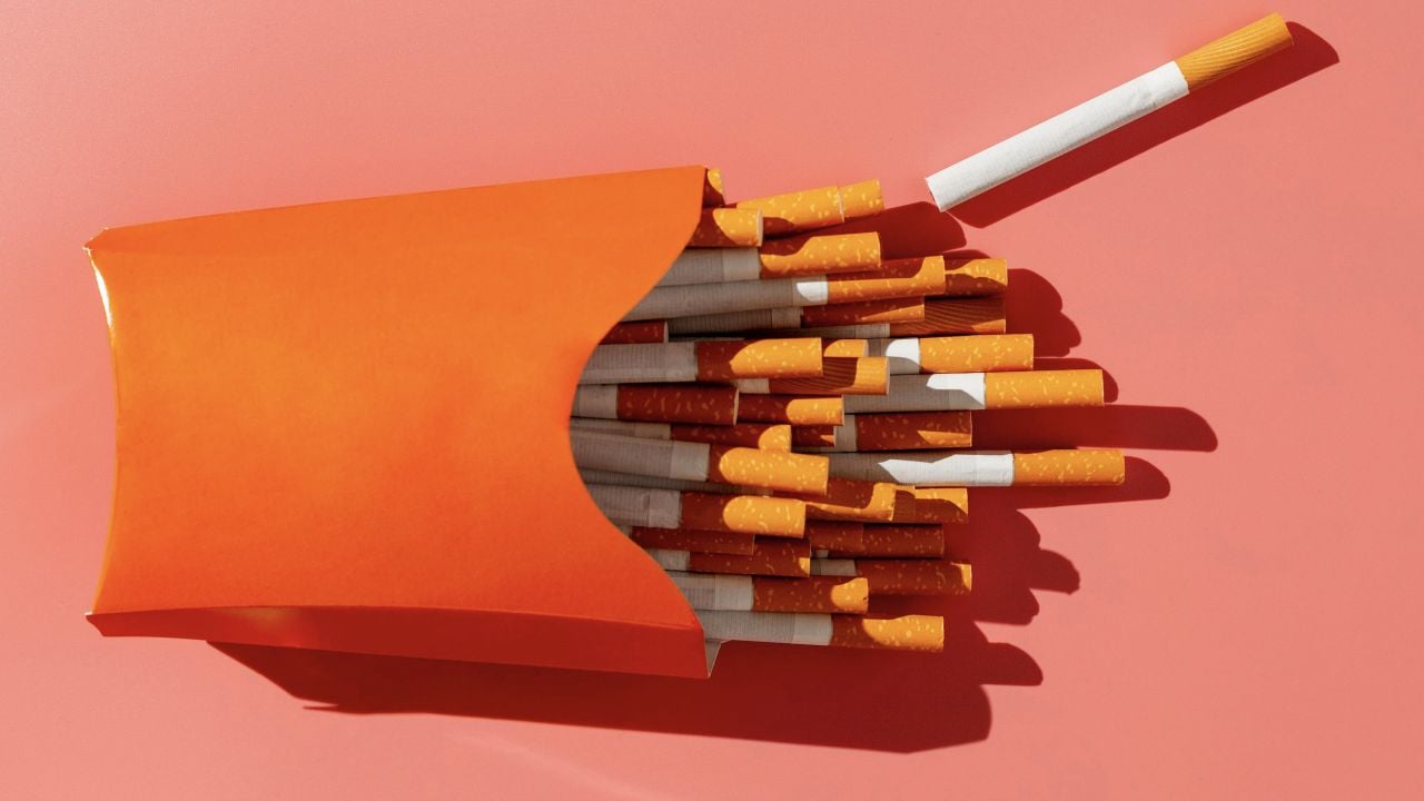 Photograph: orange pack overflowing with cigarettes on coral background, one loose