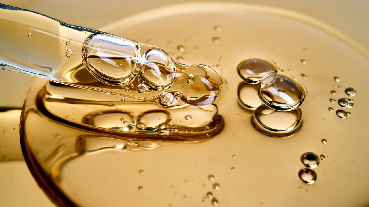 Photograph of a glass dropper releasing golden viscous oil with air bubbles