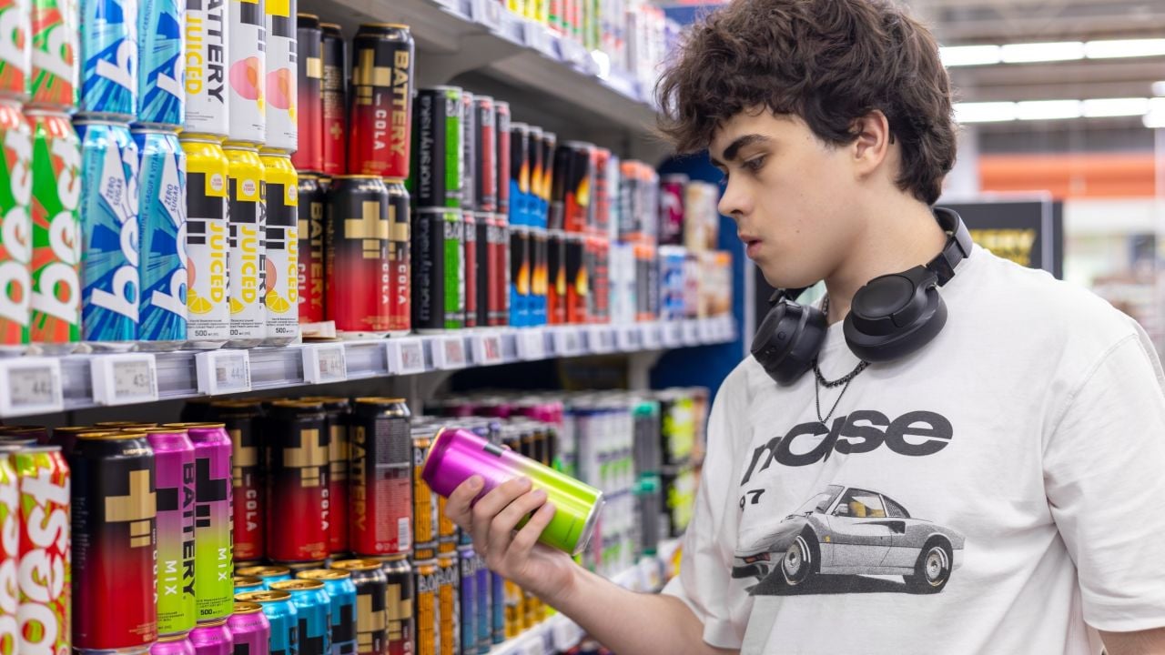 Teenage boy in headphones examining colorful drink can on supermarket shelf