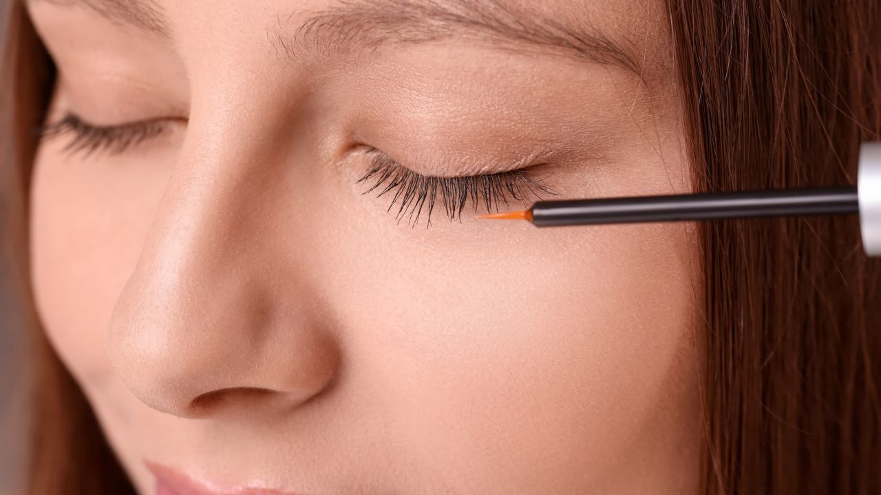 Close-up photograph of woman with closed eye applying liquid eyeliner to upper lashes